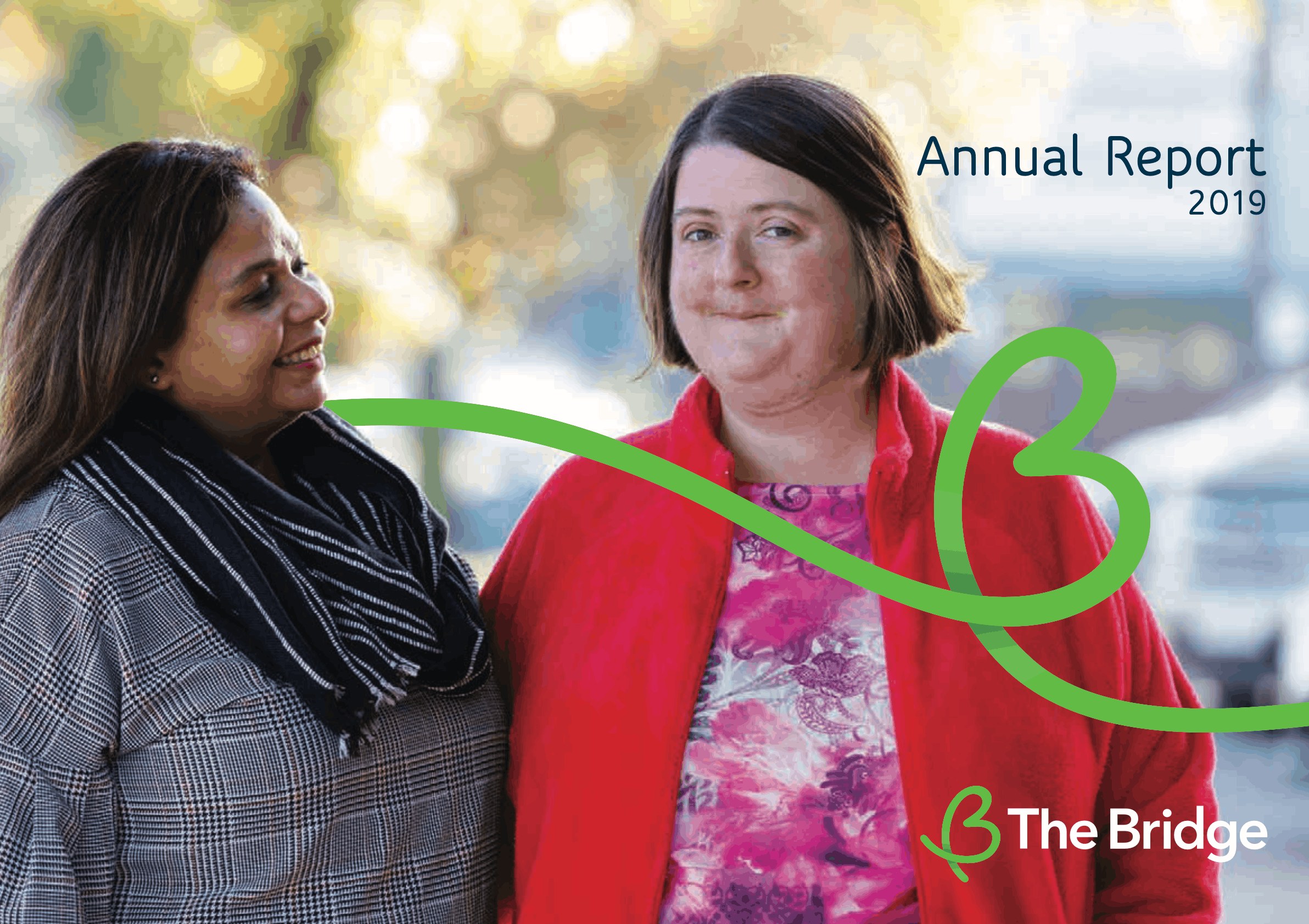 Two women stand together outdoors; The Bridge Annual Report 2019 cover with green logo swirl