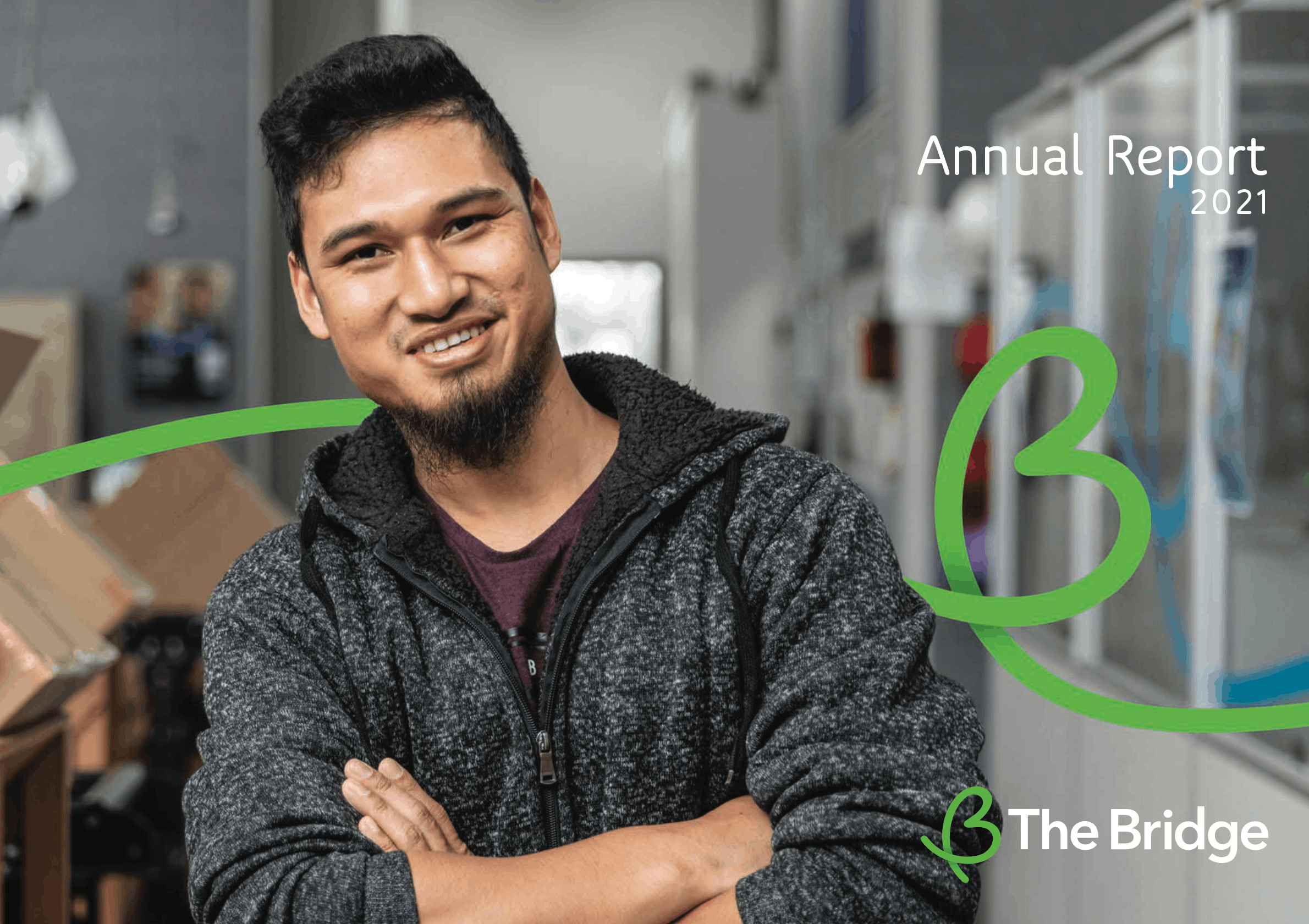 Man in grey hoodie smiling in workshop, cover of The Bridge Annual Report 2021