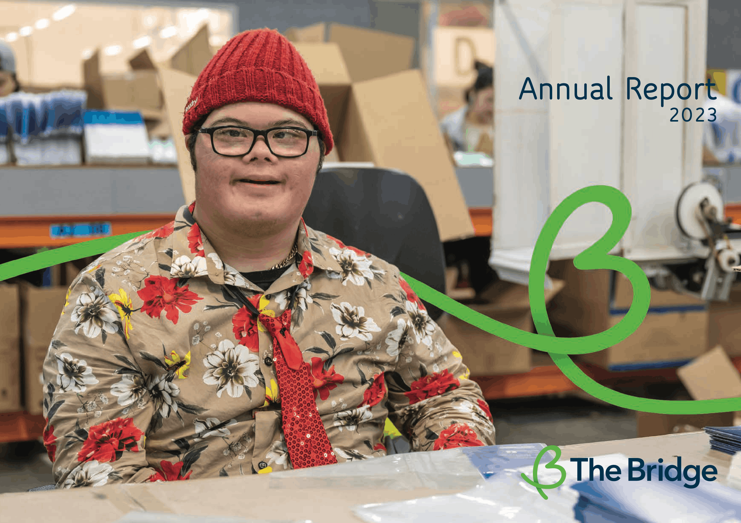 Man in red beanie and floral shirt smiling in a warehouse; The Bridge Annual Report 2023 cover