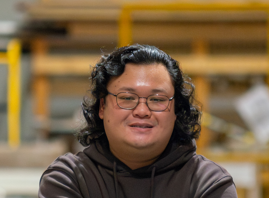 Tony wearing a brown hoodie, smiling in a warehouse setting.