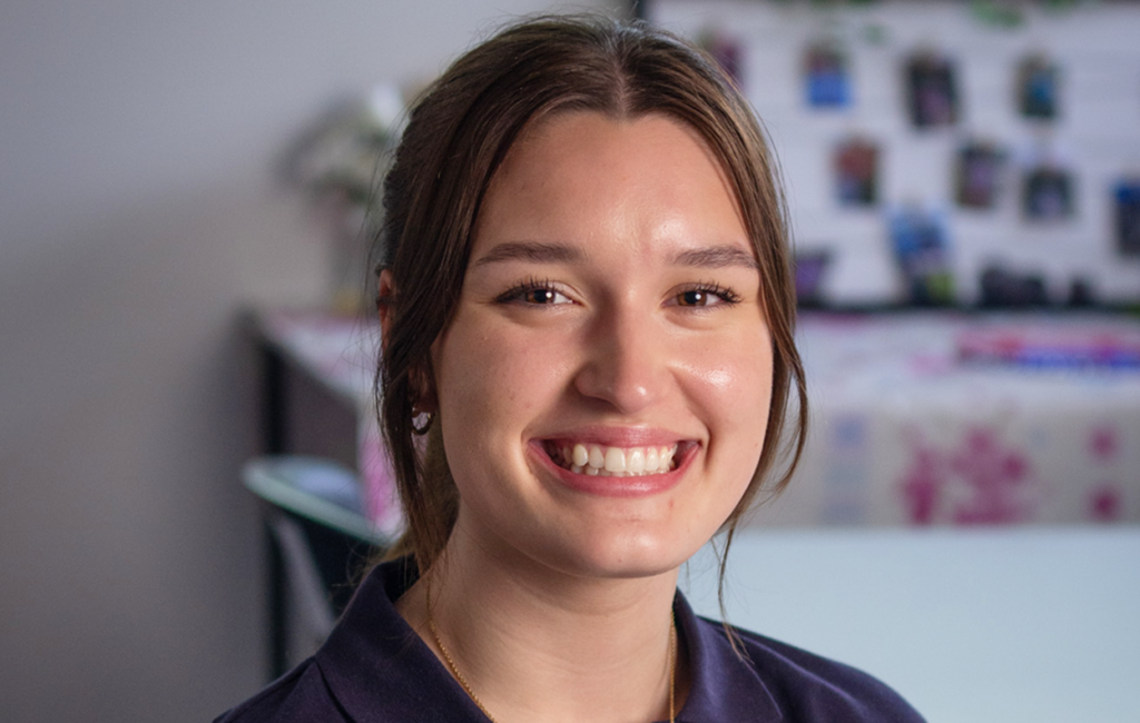 Woman with brown hair smiling at the camera, wearing a navy top, indoors.