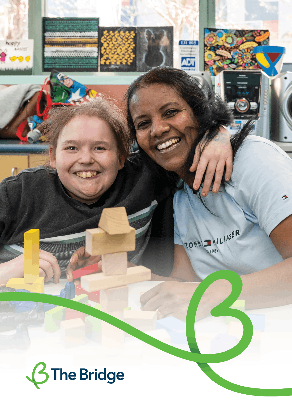 Two smiling people lean together over a table with wooden blocks, arm around shoulder, in a room with artwork.