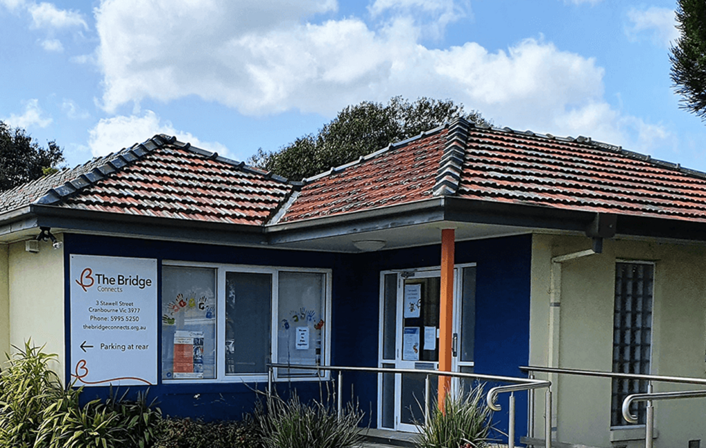 Single-storey building with tiled roof, sign reading The Bridge Connects, entrance with handrail ramp.