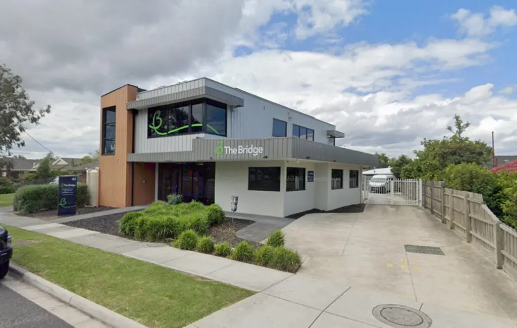 Two-storey building with 'The Bridge' signage, front garden, driveway and gated car park.