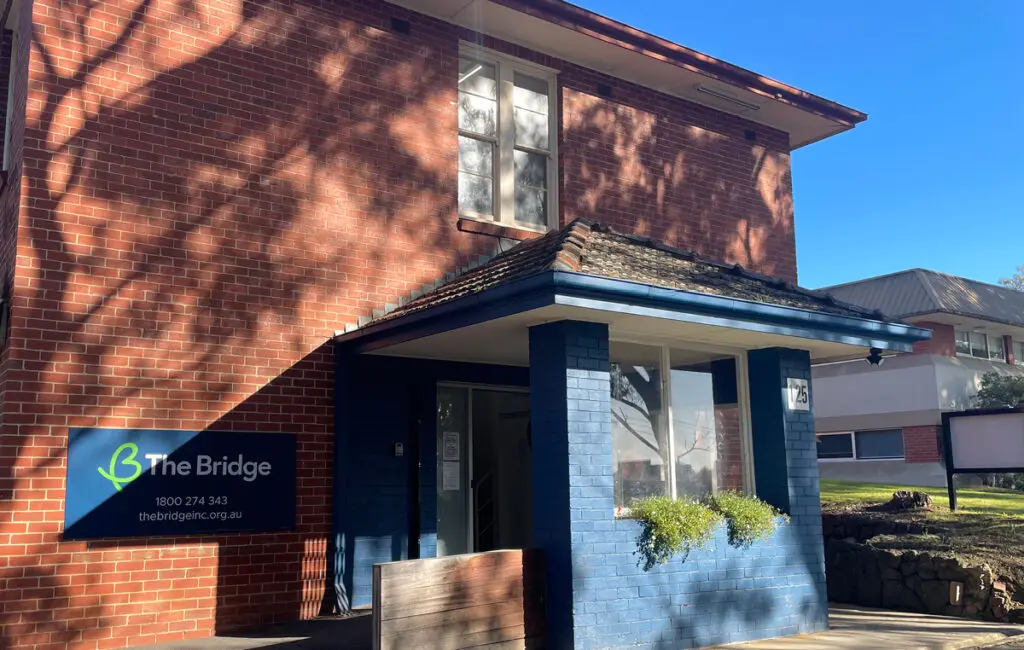 Brick building entrance with sign reading 'The Bridge, 1800 274 343, thebridgeinc.org.au'