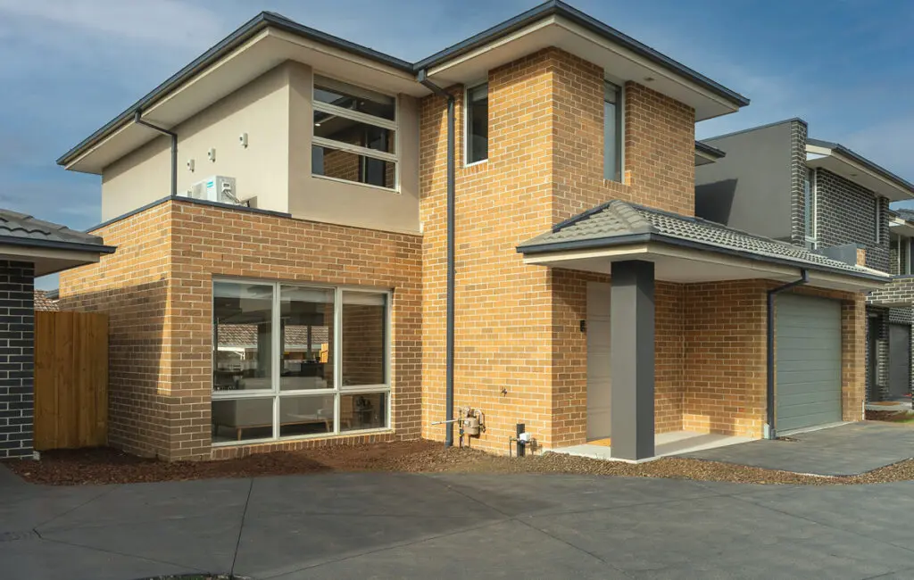 Two-storey brick house with white door, garage, front porch, and paved driveway.