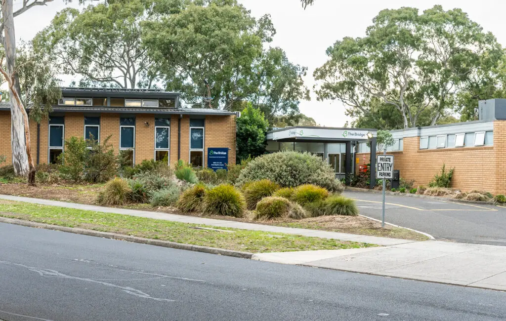 The Bridge brick building with entrance canopy, garden beds, and a private entry parking sign.
