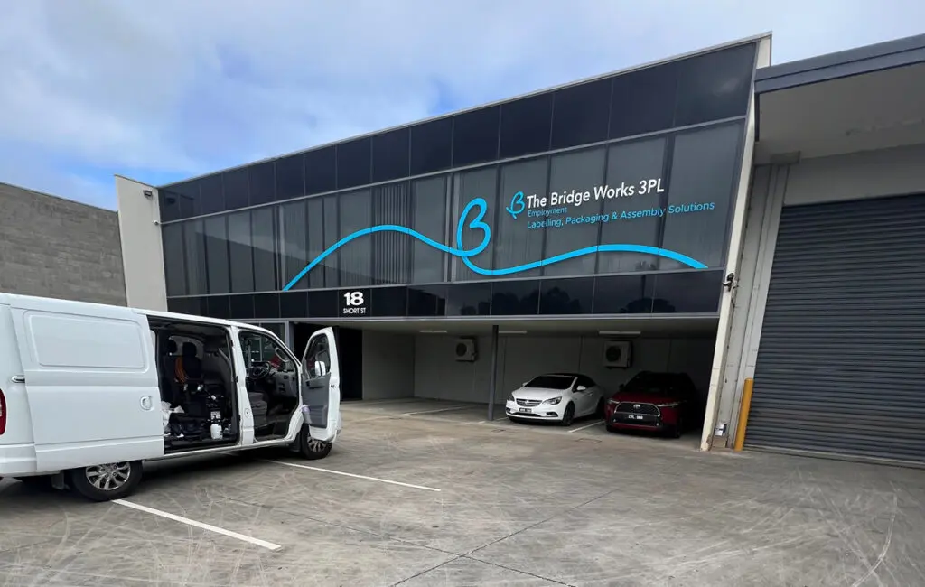 Bridge Works 3PL building at 18 Short St, with roller door, cars parked under, and a white van in the carpark