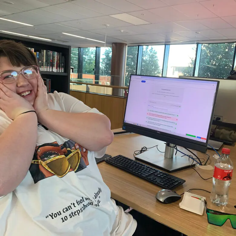 Person smiling with hands on cheeks at a desk, computer screen showing a completed quiz result behind them.