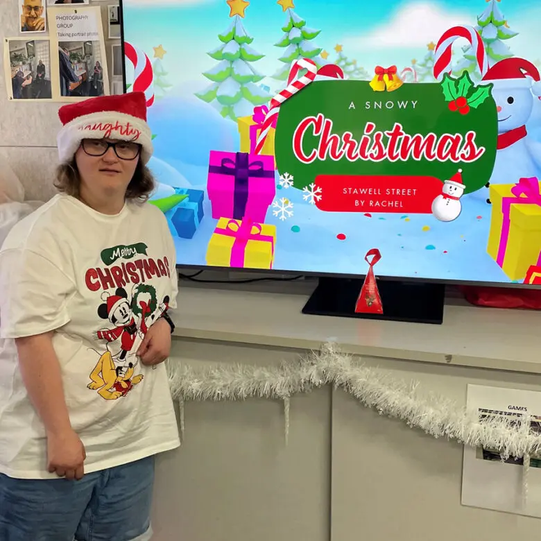 Person in Santa hat and Christmas T-shirt beside TV screen showing 'A Snowy Christmas' title slide
