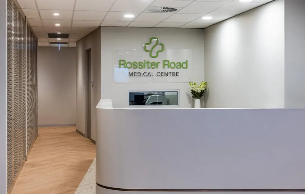 Reception desk with Rossiter Road Medical Centre sign and green cross logo, hallway to the left