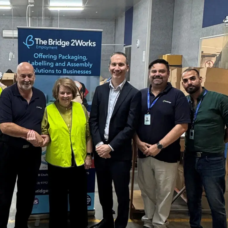 Five people stand together in a warehouse beside a Bridge 2Works Employment banner and boxes.