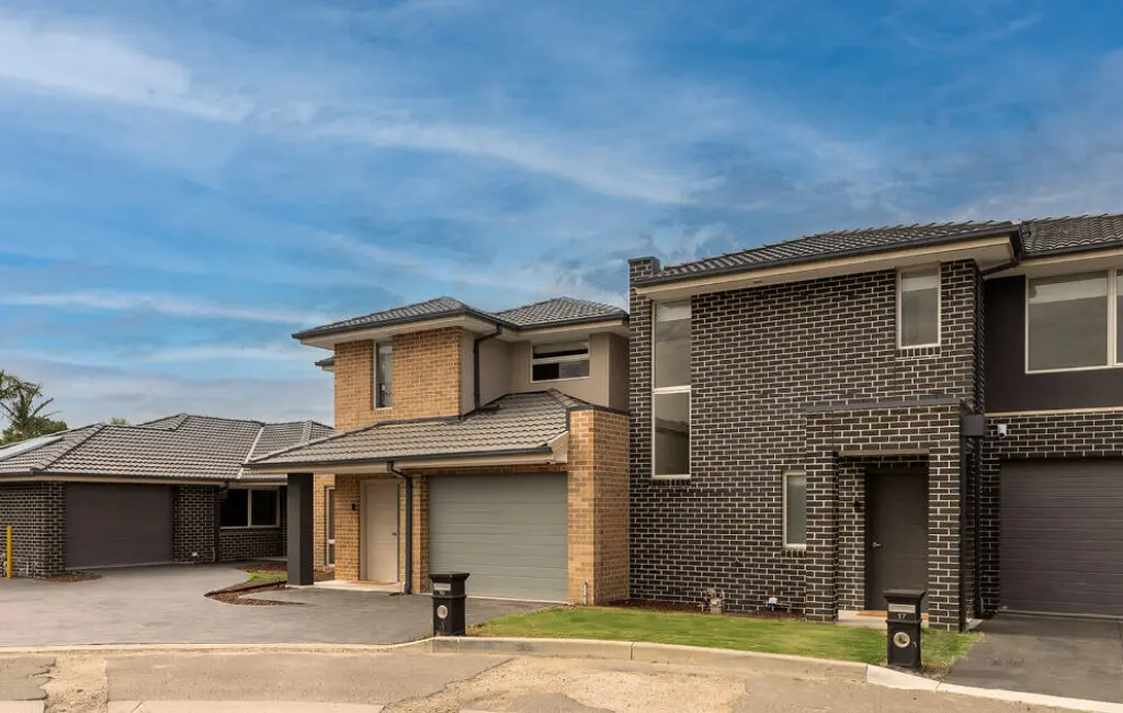 Row of modern two-storey brick townhouses with garages, driveways and letterboxes under a blue sky