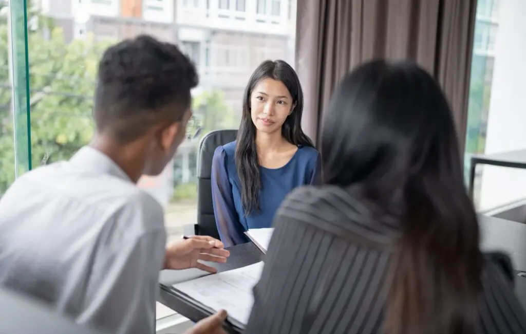 Woman sits across a table from two people, with documents open in front of them during a meeting.