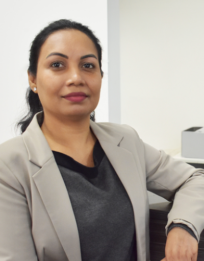 Woman with dark hair wearing a grey blazer over a dark top, seated in an office.