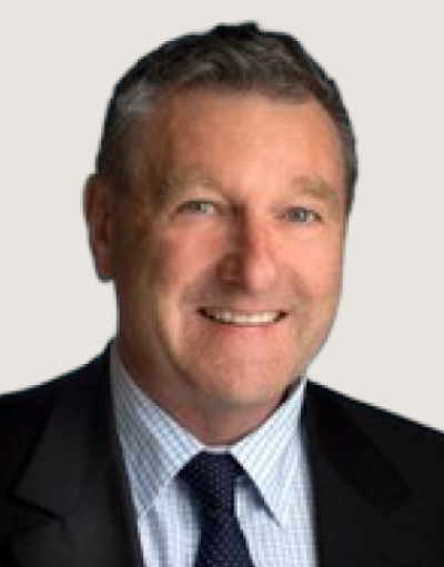 Man with grey hair smiling, wearing a dark suit, checked shirt, and navy patterned tie.