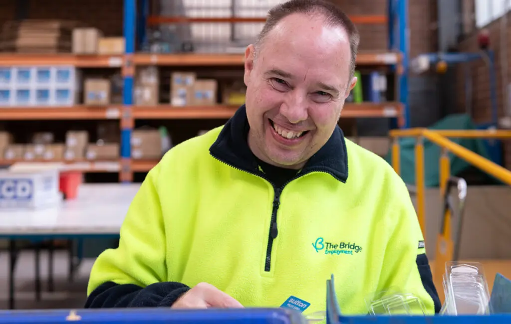 Person sorting products at a warehouse workstation, wearing a high-visibility The Bridge Employment uniform.