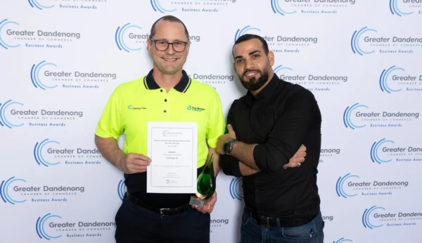 Two men holding a certificate and trophy in front of a Greater Dandenong Chamber of Commerce backdrop