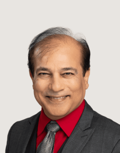 Man smiling in a grey suit, red shirt, and grey tie, against a plain light background.