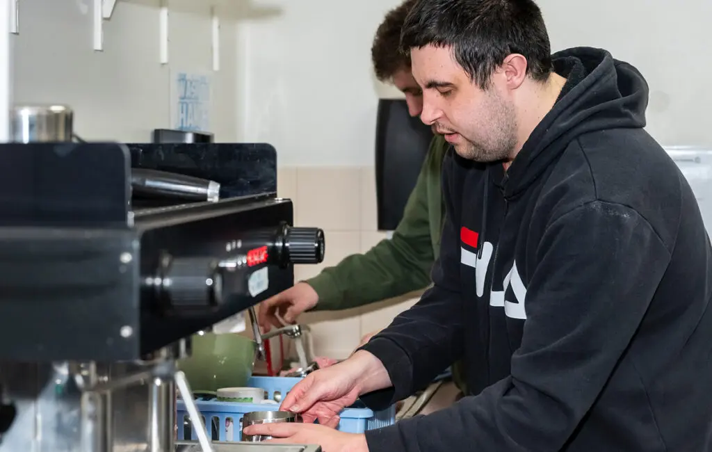 Person preparing coffee at a commercial espresso machine in a café kitchen.