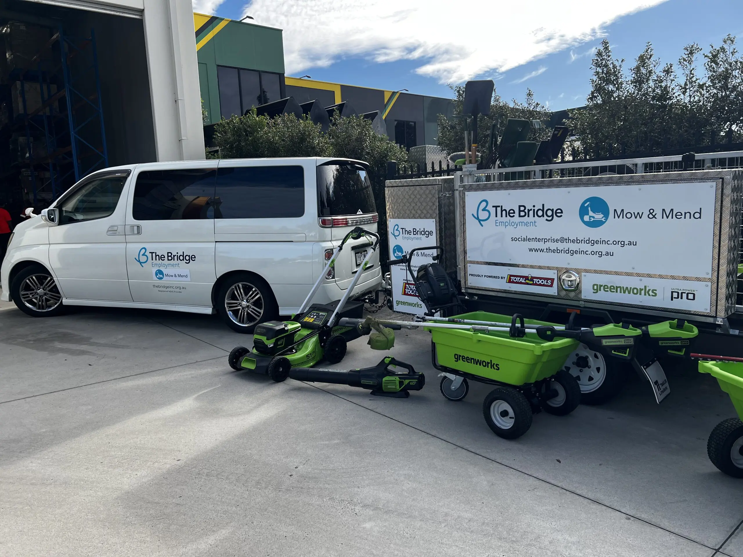 White van and trailer branded 'The Bridge Employment Mow & Mend' with lawn mower, blower and green cart parked outside