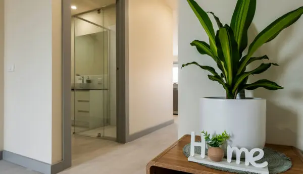 Hallway with potted plant and 'Home' decor on wooden table beside a doorway to a glass-walled bathroom.