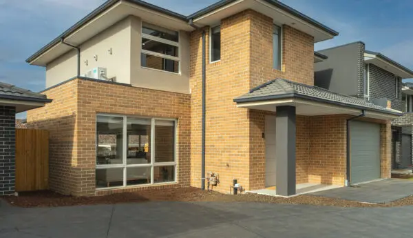 Two-storey brick house with white front door, covered porch, garage, and driveway.
